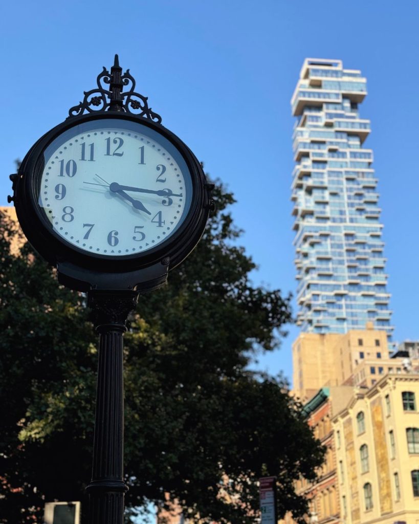 Calle de Tribeca con su icónico reloj de hierro y el edificio Jenga al fondo, barrio exclusivo recomendado para alojarse en Nueva York.