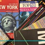 Composición horizontal de dos guías de viaje, mapas de subte y bus de Nueva York junto a un anotador temático de NYC sobre una mesa.