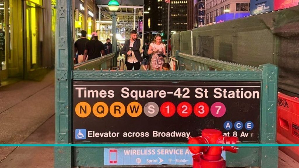 Cartel informativo en la estación de metro Times Square - 42 St en Nueva York, mostrando los círculos de colores de las líneas 1, 2, 3, 7, N, Q, R, W y S sobre un fondo negro.