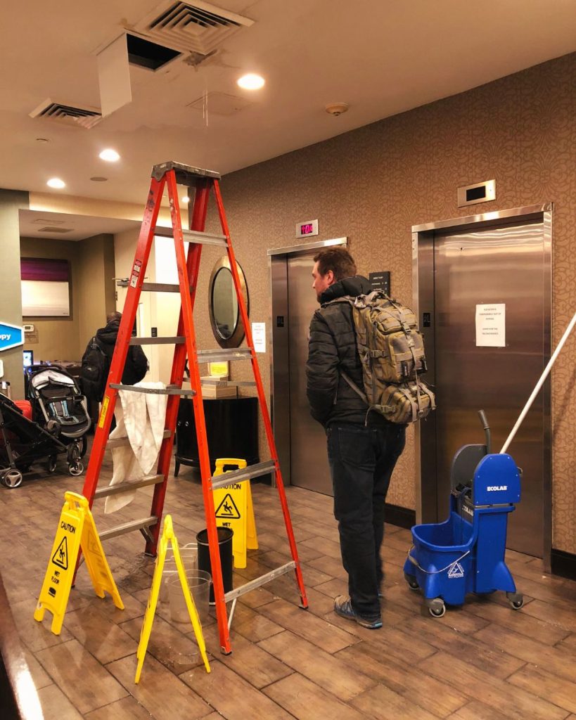 Hall de ascensores del hotel Hampton Inn 35th ST con agua filtrándose desde el techo y baldes en el suelo debido a la rotura de un caño en el piso superior.
