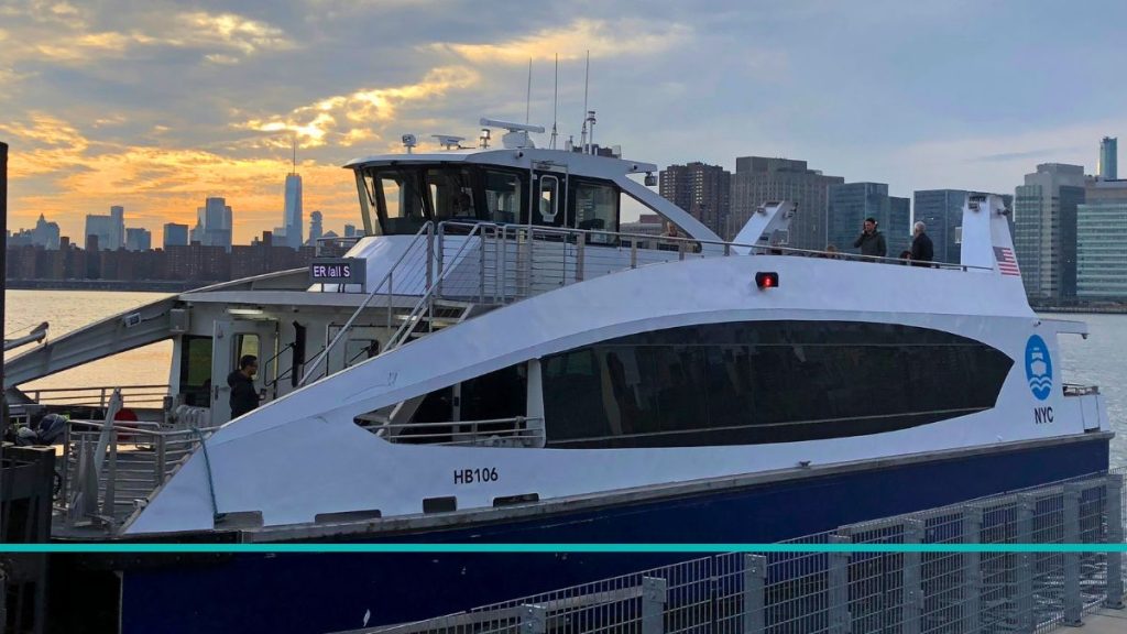 Un barco de la flota de NYC Ferry navegando por el East River con los rascacielos de Manhattan y el cielo azul de fondo