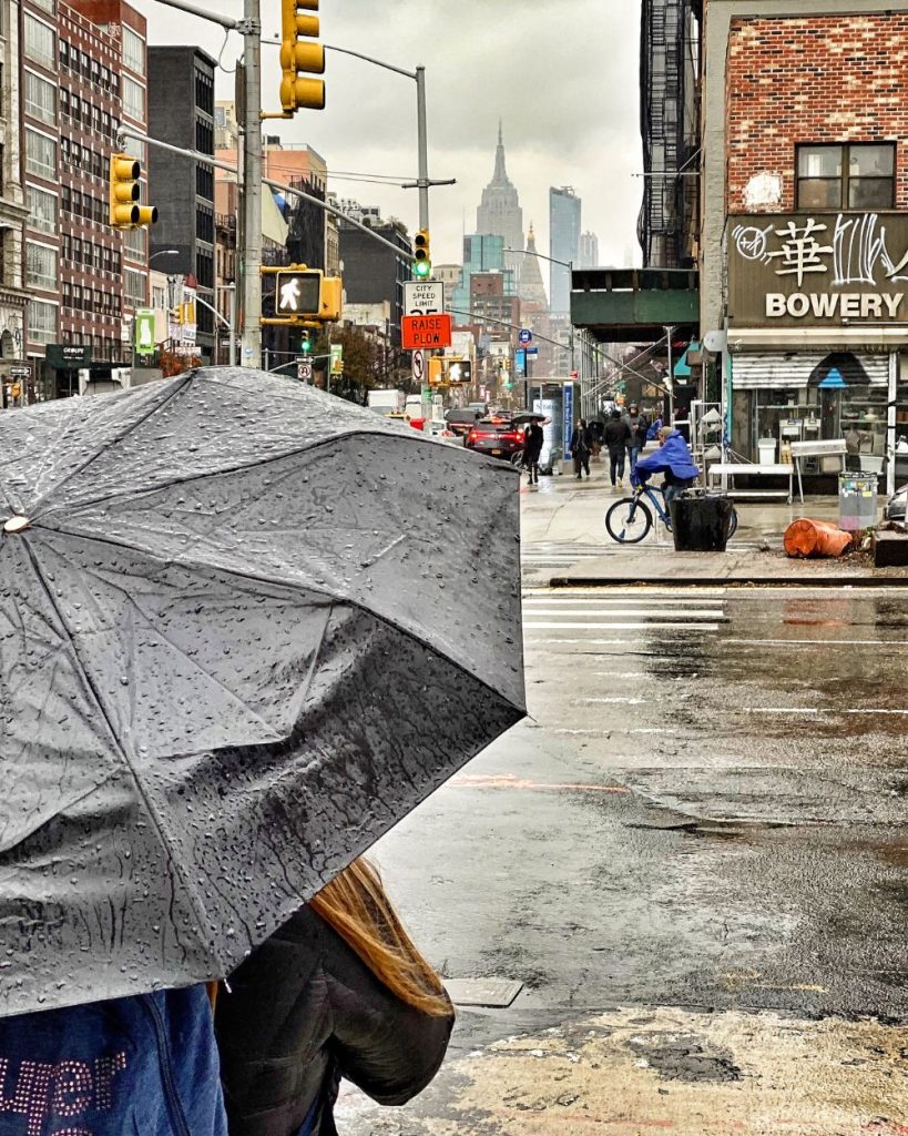Una mujer de espaldas caminando con un paraguas bajo la lluvia por las calles decoradas con carteles de Chinatown, Nueva York.